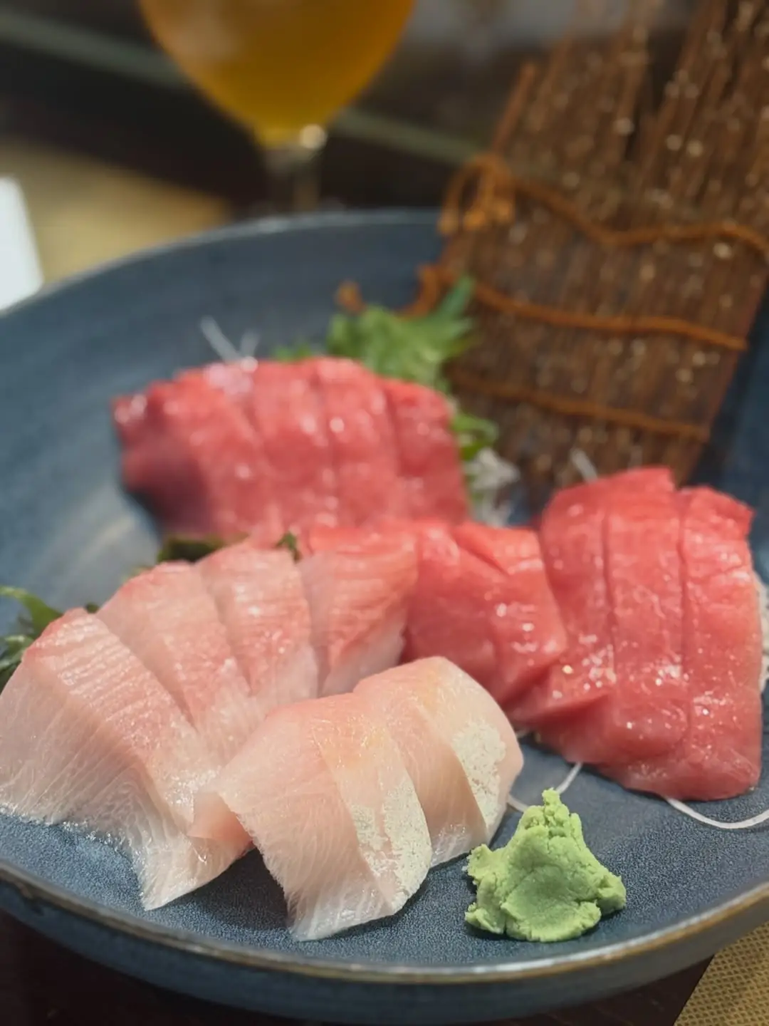 Sliced tuna and yellowtail sashimi on a dark plate with a dollop of wasabi