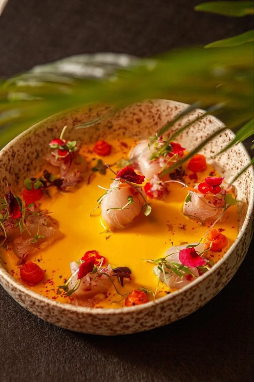 A round bowl of sliced fish in a bright yellow sauce with red garnishes