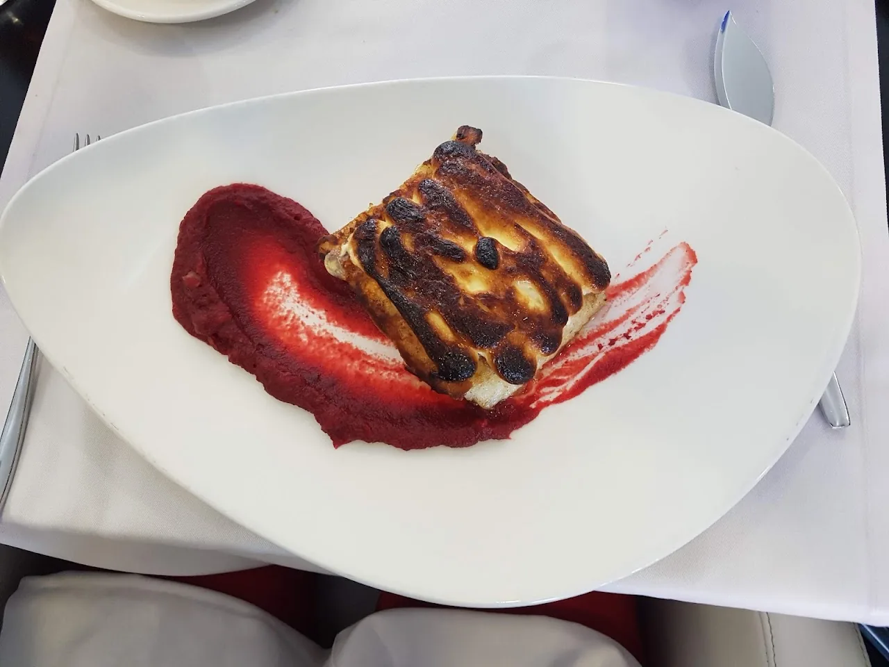 A grilled dessert square with a red berry sauce swirl on a white plate