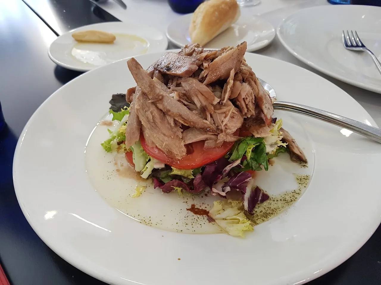 A plate of shredded meat over a tomato and lettuce salad