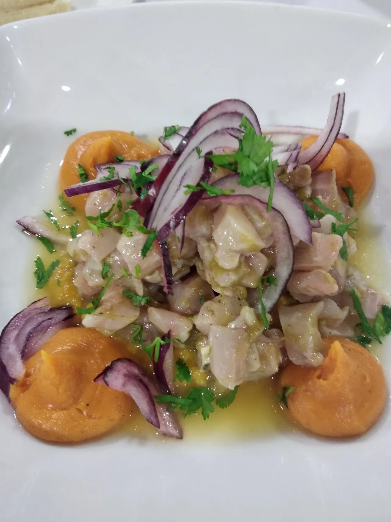 A ceviche dish with white fish, red onion, cilantro, and orange segments