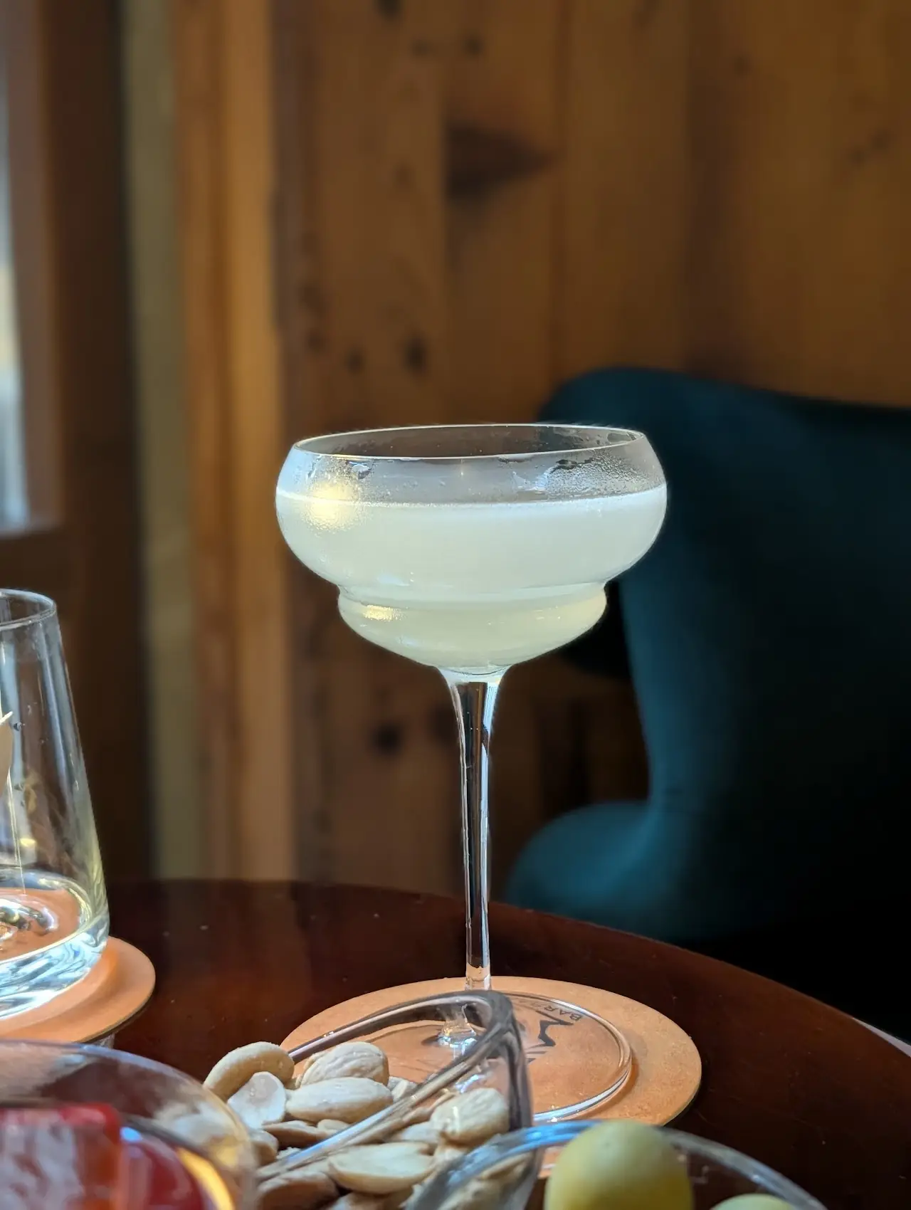 A margarita in a coupe glass on a bar table, with pistachios nearby.