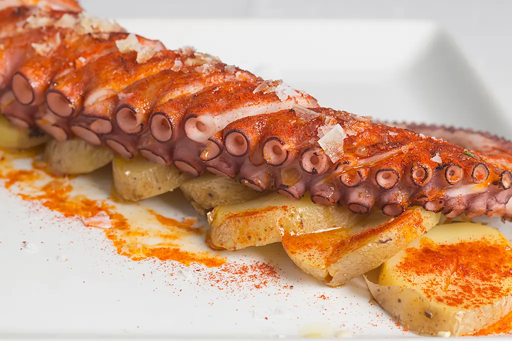 Grilled octopus slices dusted with paprika, served over sliced potatoes on a white plate at Mirando al Mar