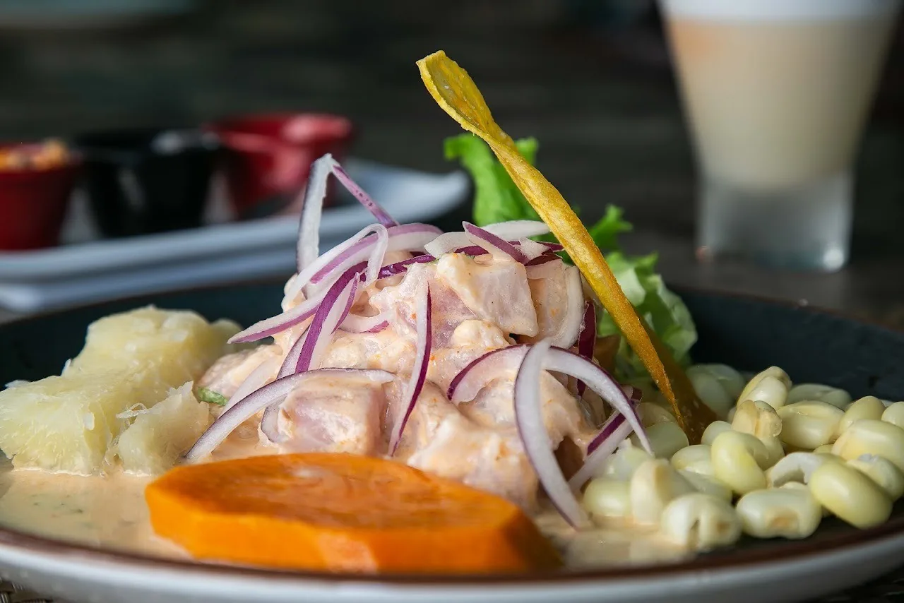 A plate of ceviche with red onion, sweet potato and large white corn kernels