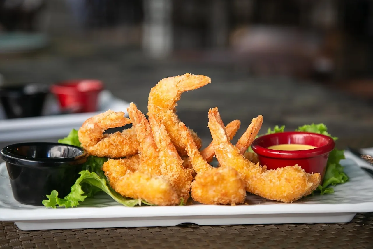 A plate of breaded fried shrimp with red and dark dipping sauces