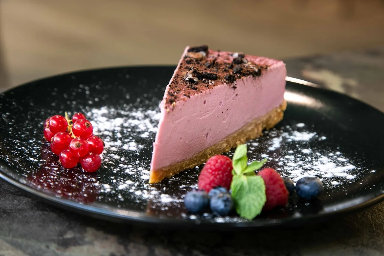 A slice of pink cheesecake topped with berries and mint