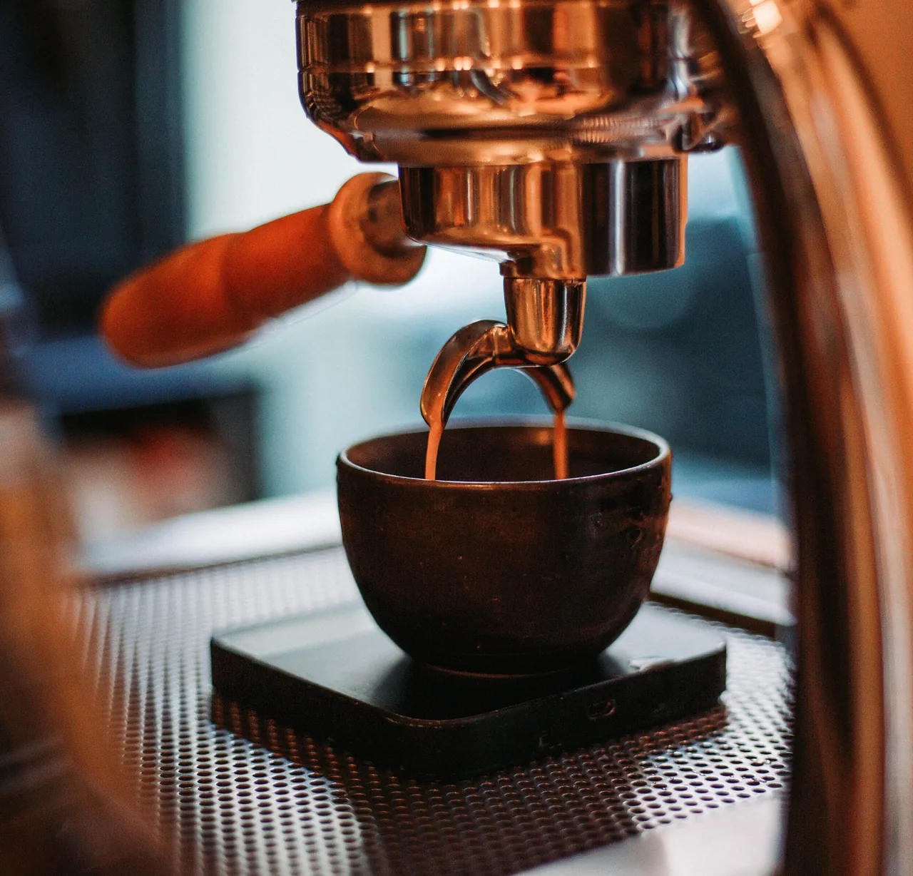 Espresso pouring from a copper portafilter into a small dark bowl on a scale