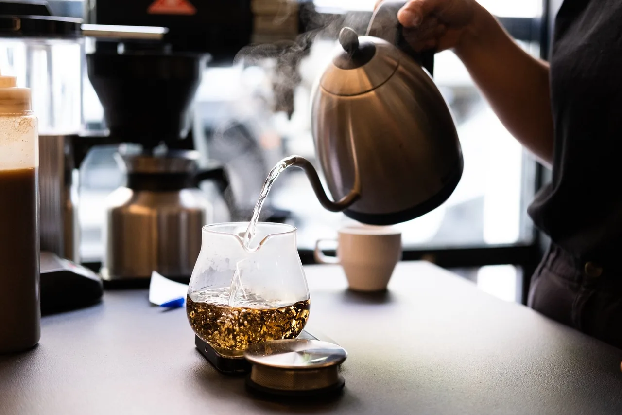 Water being poured from a gooseneck kettle into a glass pour-over server