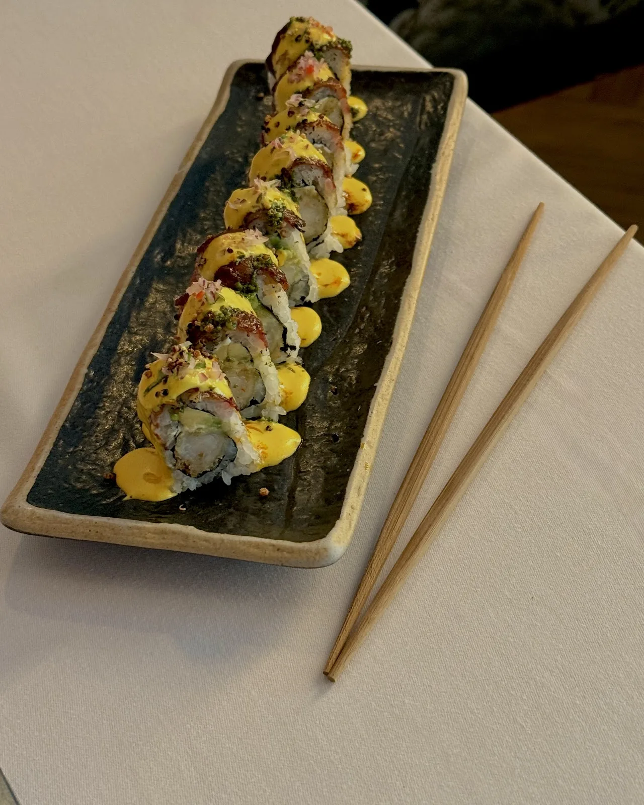 A sushi roll topped with fish roe and citrus slices, served with chopsticks
