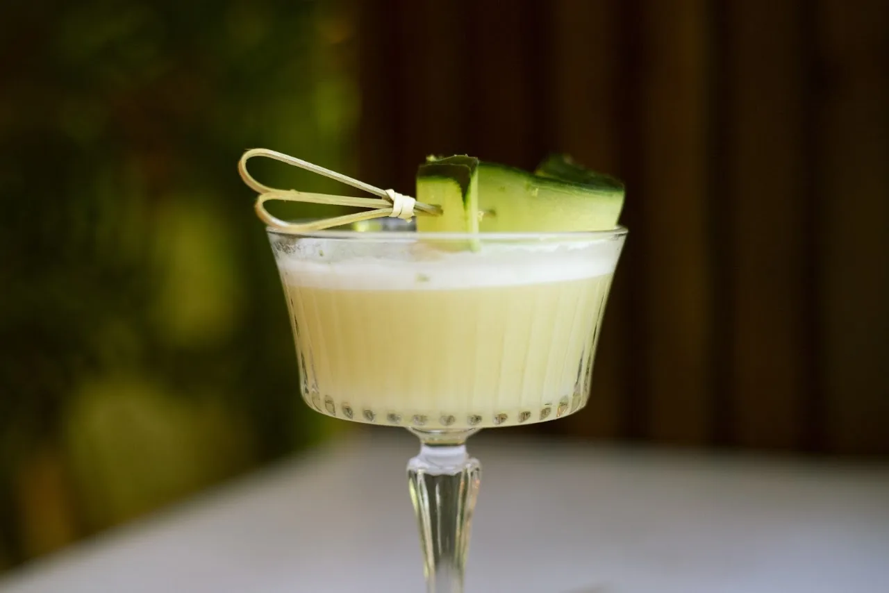 A pale yellow cocktail garnished with a cucumber ribbon