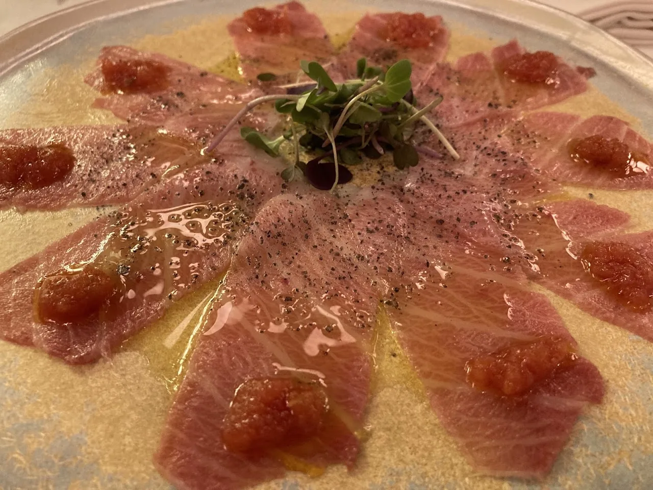 Thinly sliced tuna carpaccio arranged in a circle with pepper and sauce dots