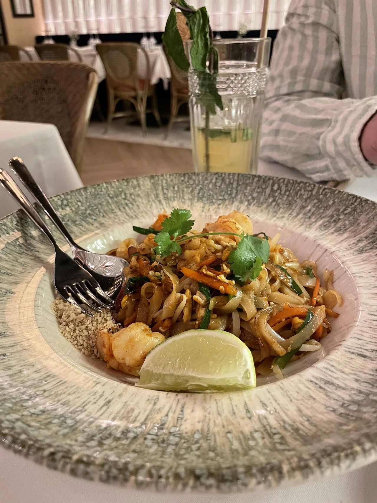 A bowl of stir-fried noodles with shrimp and a lime wedge