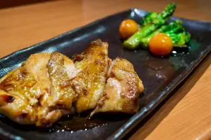Grilled chicken skewers plated with broccolini and cherry tomatoes on a black dish