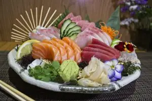 A platter of assorted sashimi including salmon, tuna, and other fish with wasabi, ginger, and edible flowers