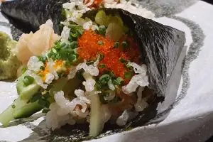 A hand roll filled with rice, cucumber, crab, and orange fish roe, garnished with chives