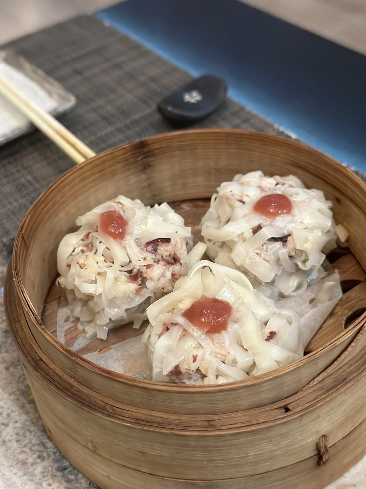 A bamboo steamer with three dumplings topped with a red garnish