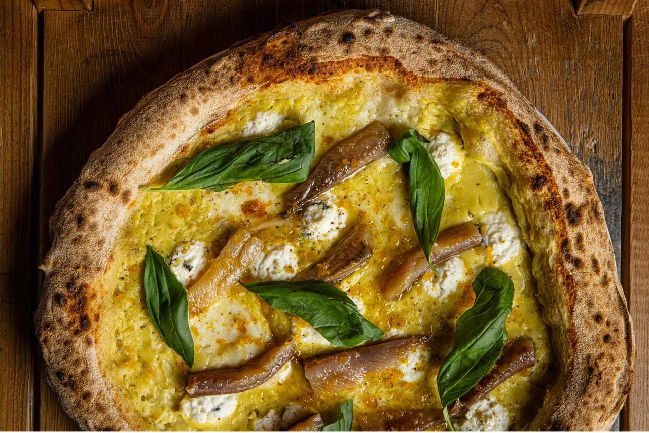 A blistered pizza topped with anchovies and basil leaves seen from above