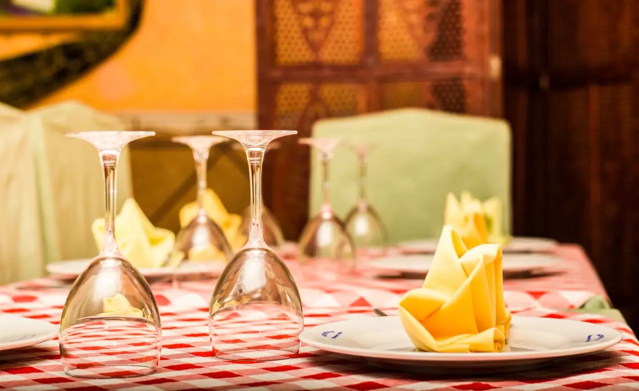 Close view of a laid table with upturned wine glasses and folded yellow napkins on a red gingham cloth by a carved wooden screen