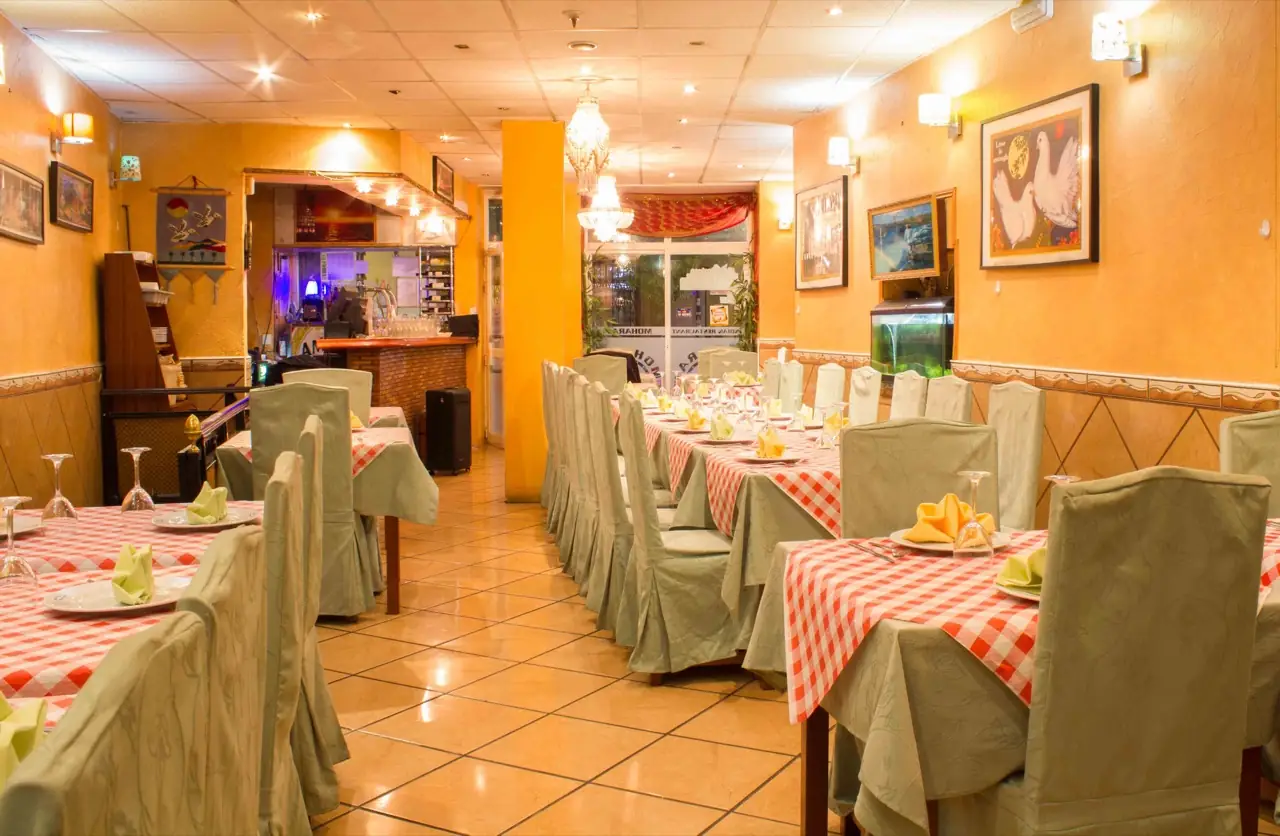 Long view of the Moharaj dining room with ochre walls, chandeliers, a fish tank and tables set with gingham cloths and green chair covers