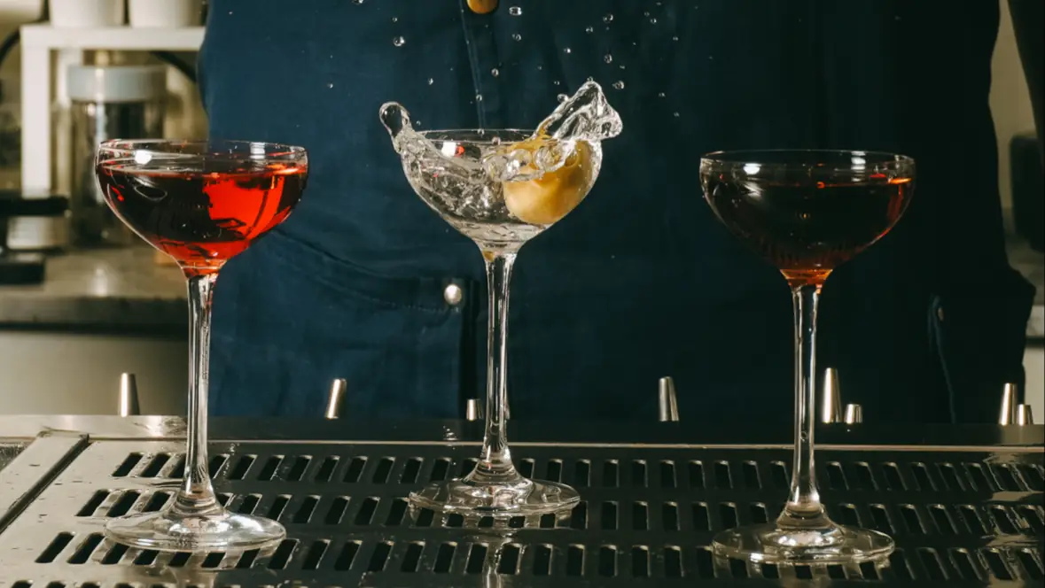 Three coupe glasses filled with red and orange cocktails on a dark bar counter.