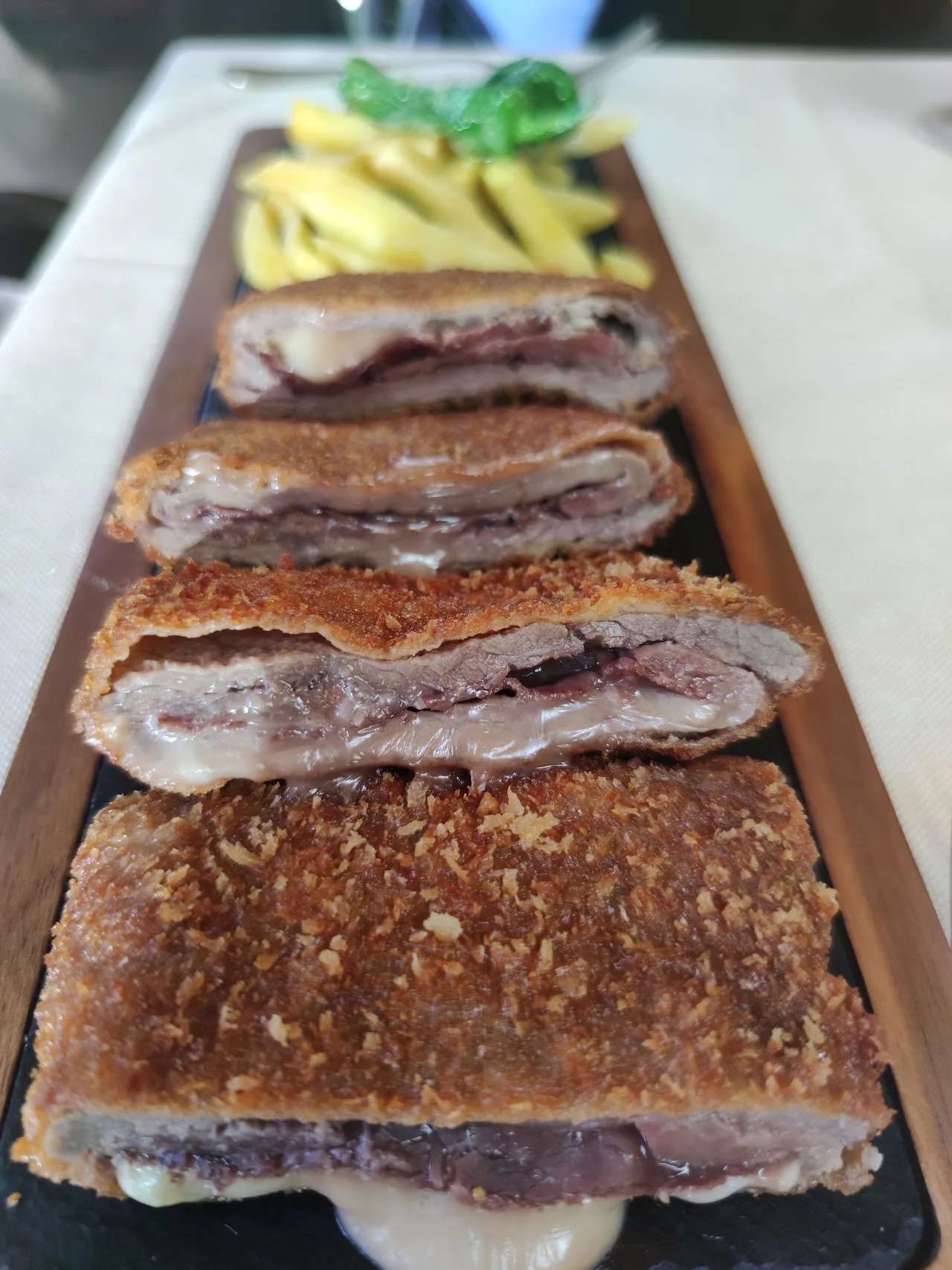 A wooden board of sliced breaded veal cachopo with melted cheese