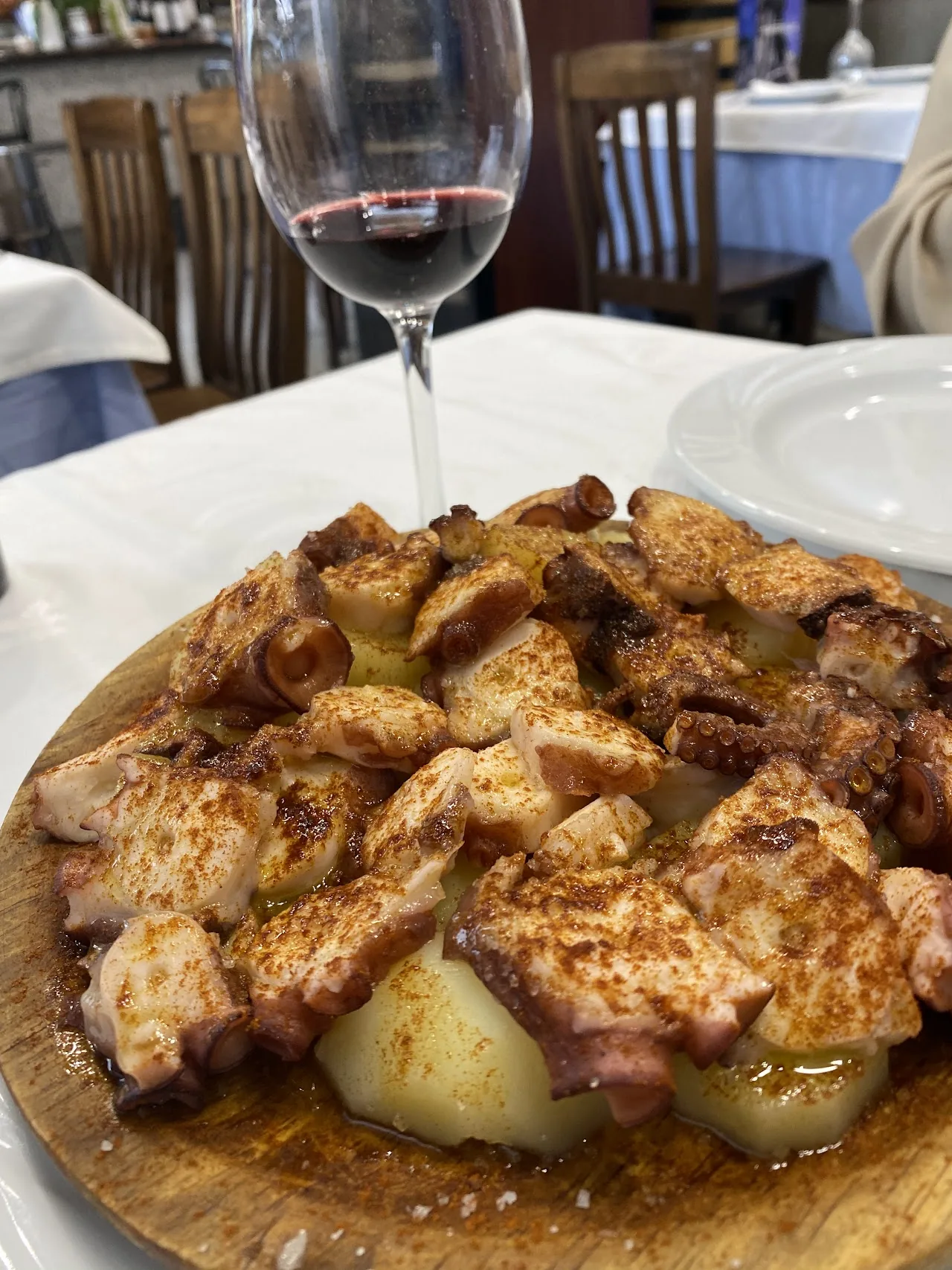 A wooden board of grilled diced pork with a wine glass in the background