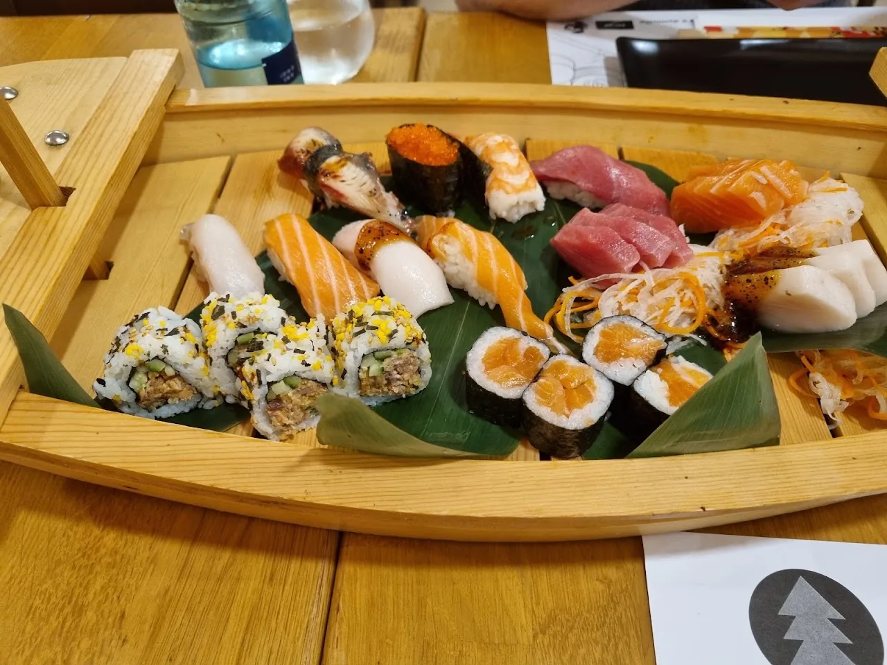 A wooden boat platter piled with assorted sushi and sashimi