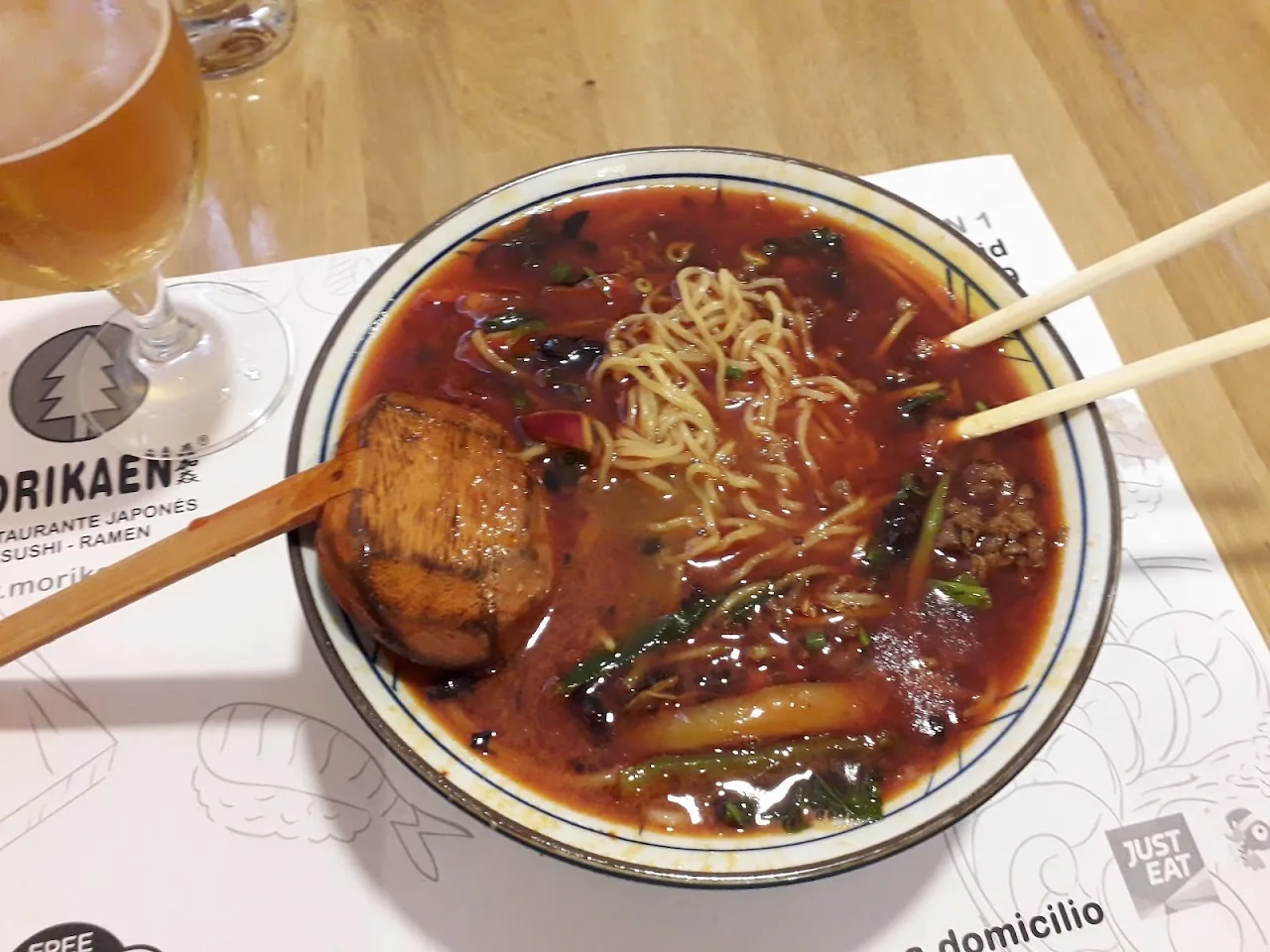 A bowl of spicy noodle soup with chopsticks resting on top