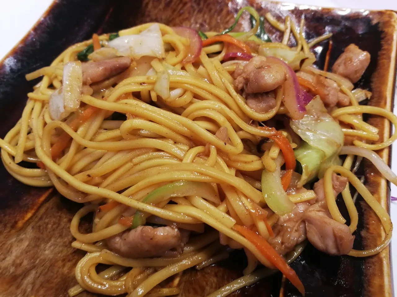 A plate of stir-fried yakisoba noodles with chicken and vegetables
