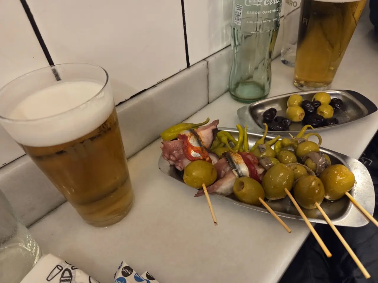Olive-and-anchovy banderilla skewers on a tin beside a beer, at Morro Fi.