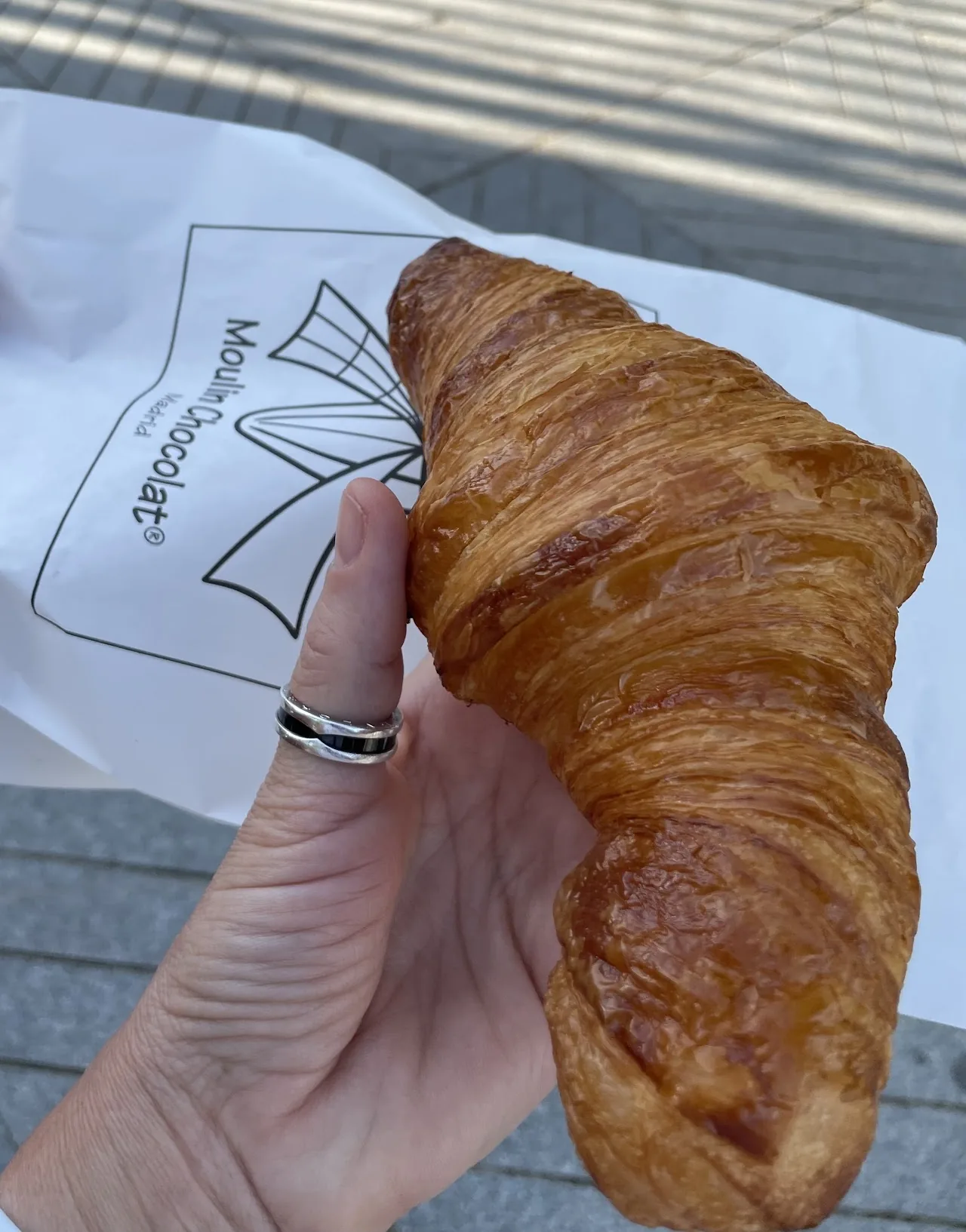 A hand holding a golden croissant outdoors