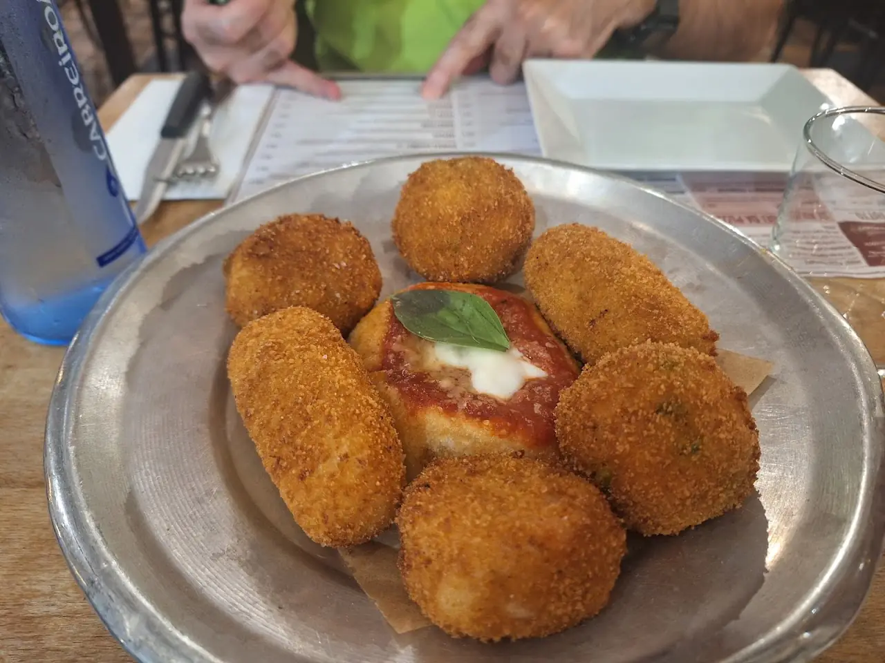 Breaded fried arancini arranged around a small dish of tomato sauce topped with basil.