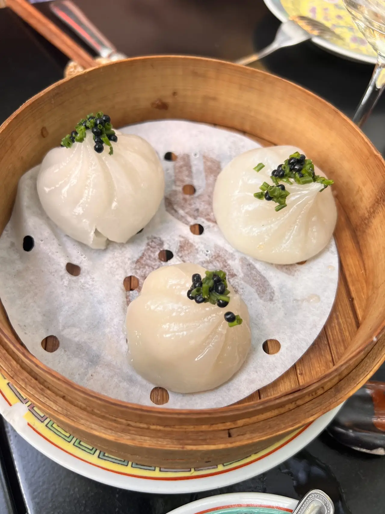 Three steamed buns in a bamboo steamer basket, garnished with chopped herbs.