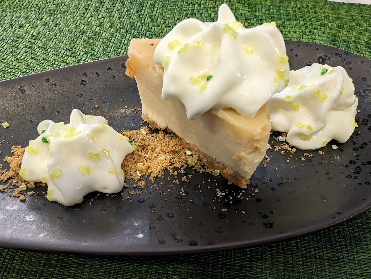 A slice of pie topped with piped whipped cream and lime zest on a dark plate.