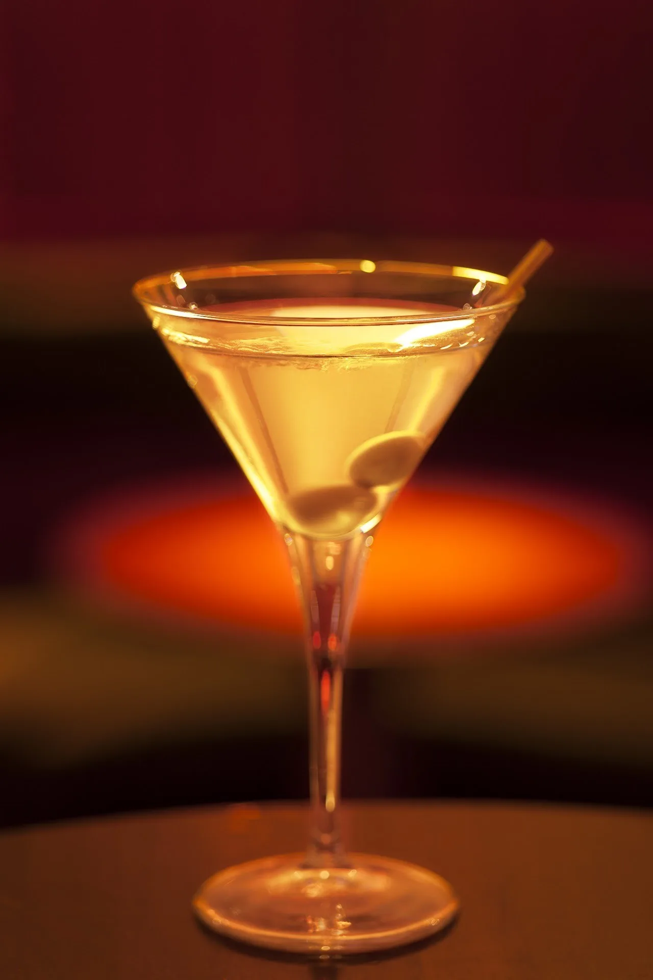 A martini glass with a pale drink and an olive against a dark warm background