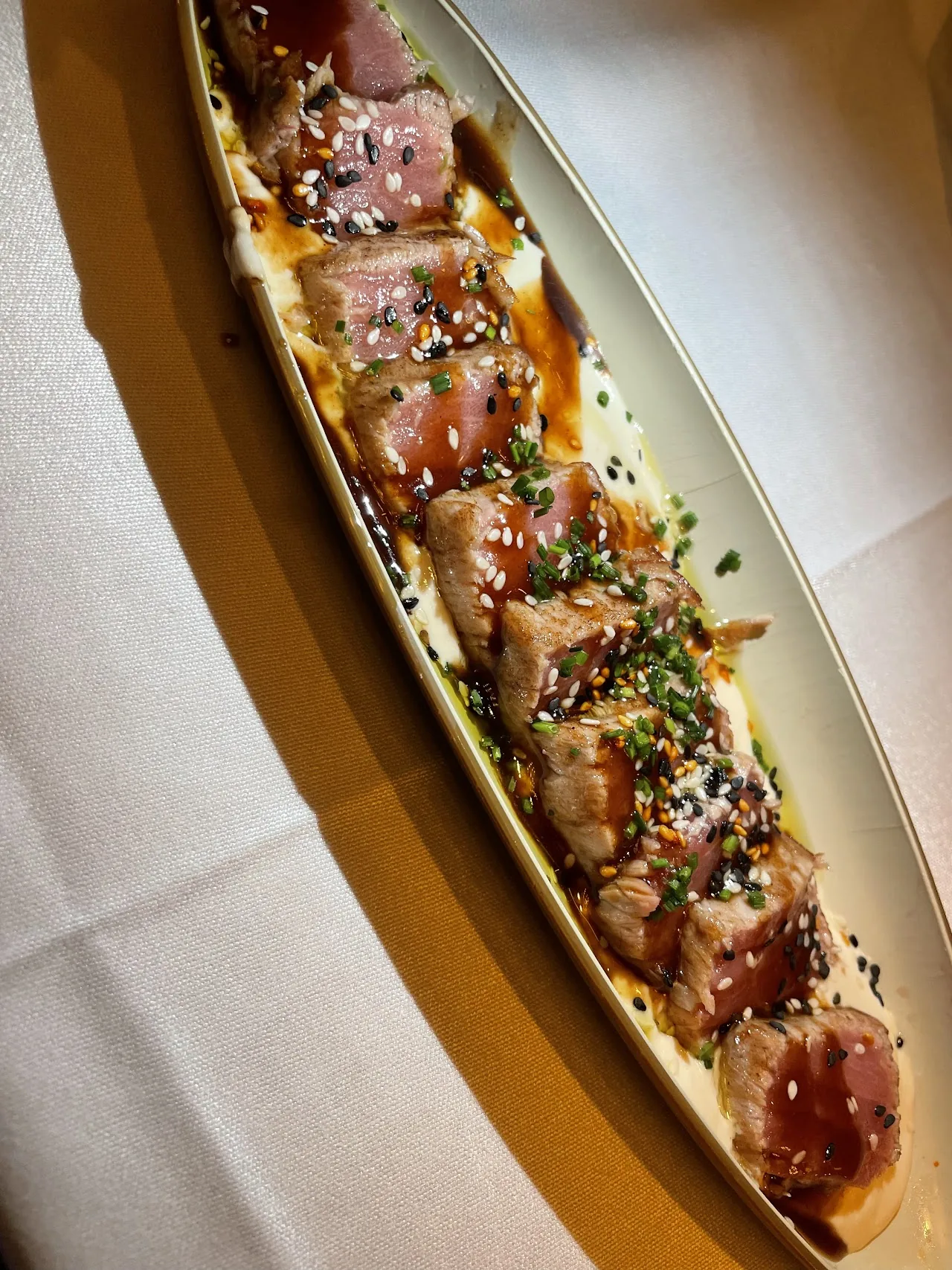 Slices of seared tuna arranged on an oval plate with sauce dots