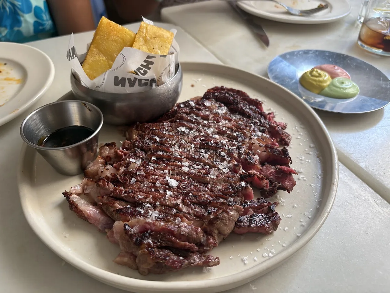 A grilled steak on a grey plate with a small dish of sauce