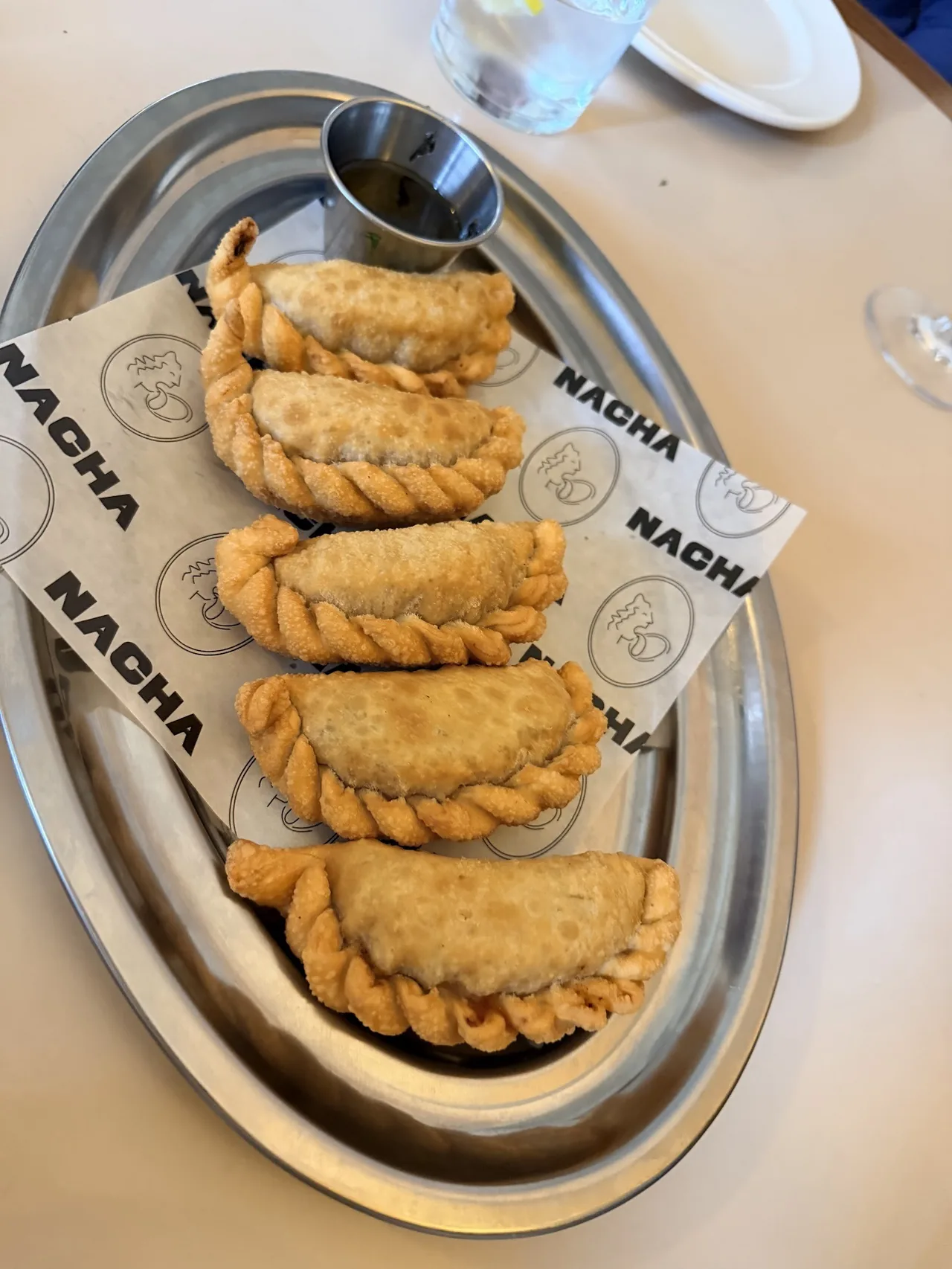 A row of baked empanadas on an oval metal tray