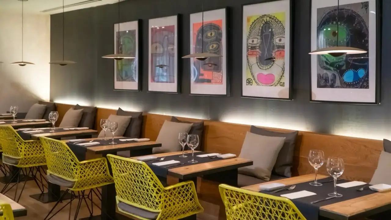 Banquette seating with yellow lattice chairs and set tables beneath five colourful framed face-motif prints