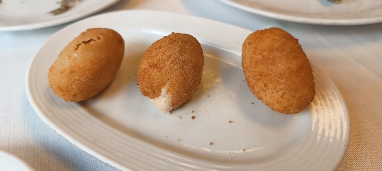 Three fried croquettes on a plate, one broken open