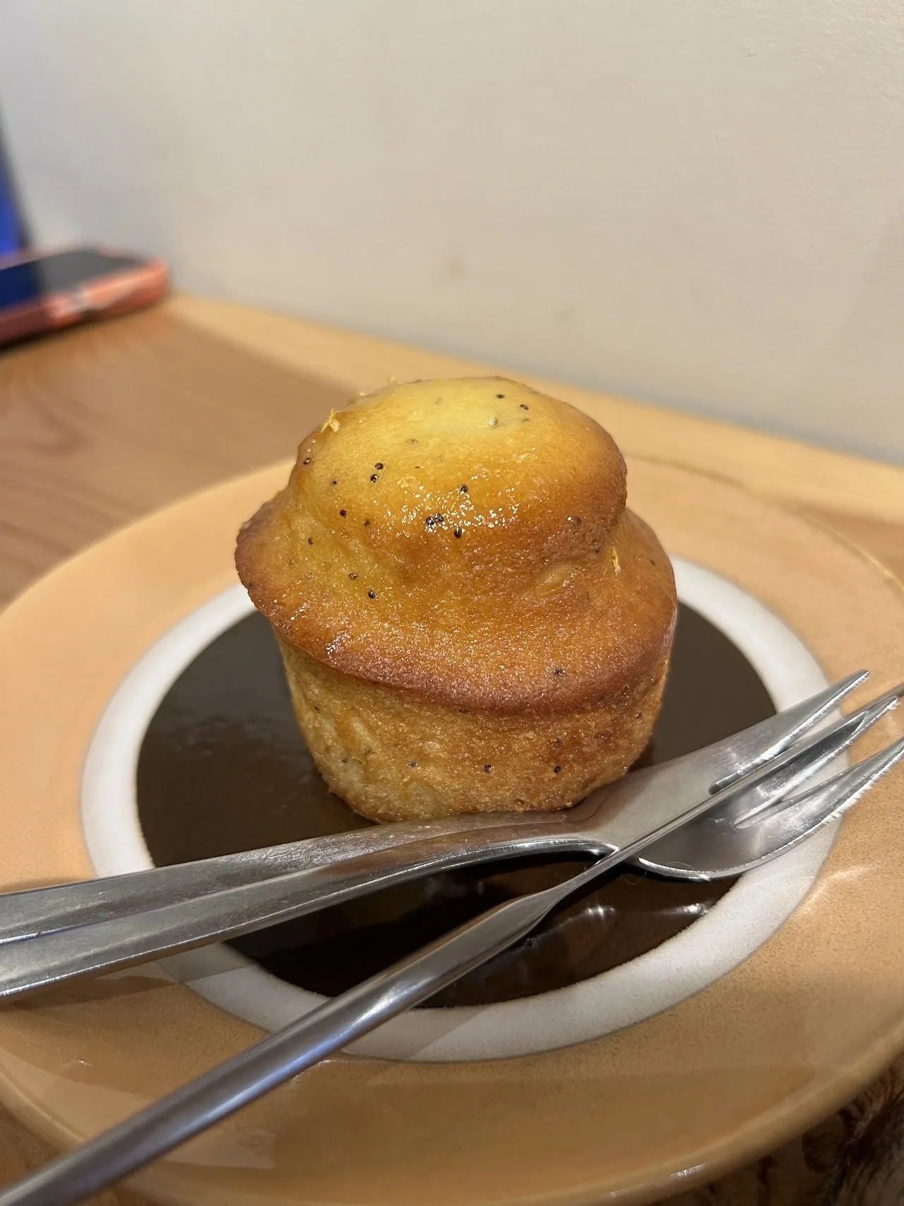 A muffin resting on a small saucer with a dark drink in a cup on a wooden tray