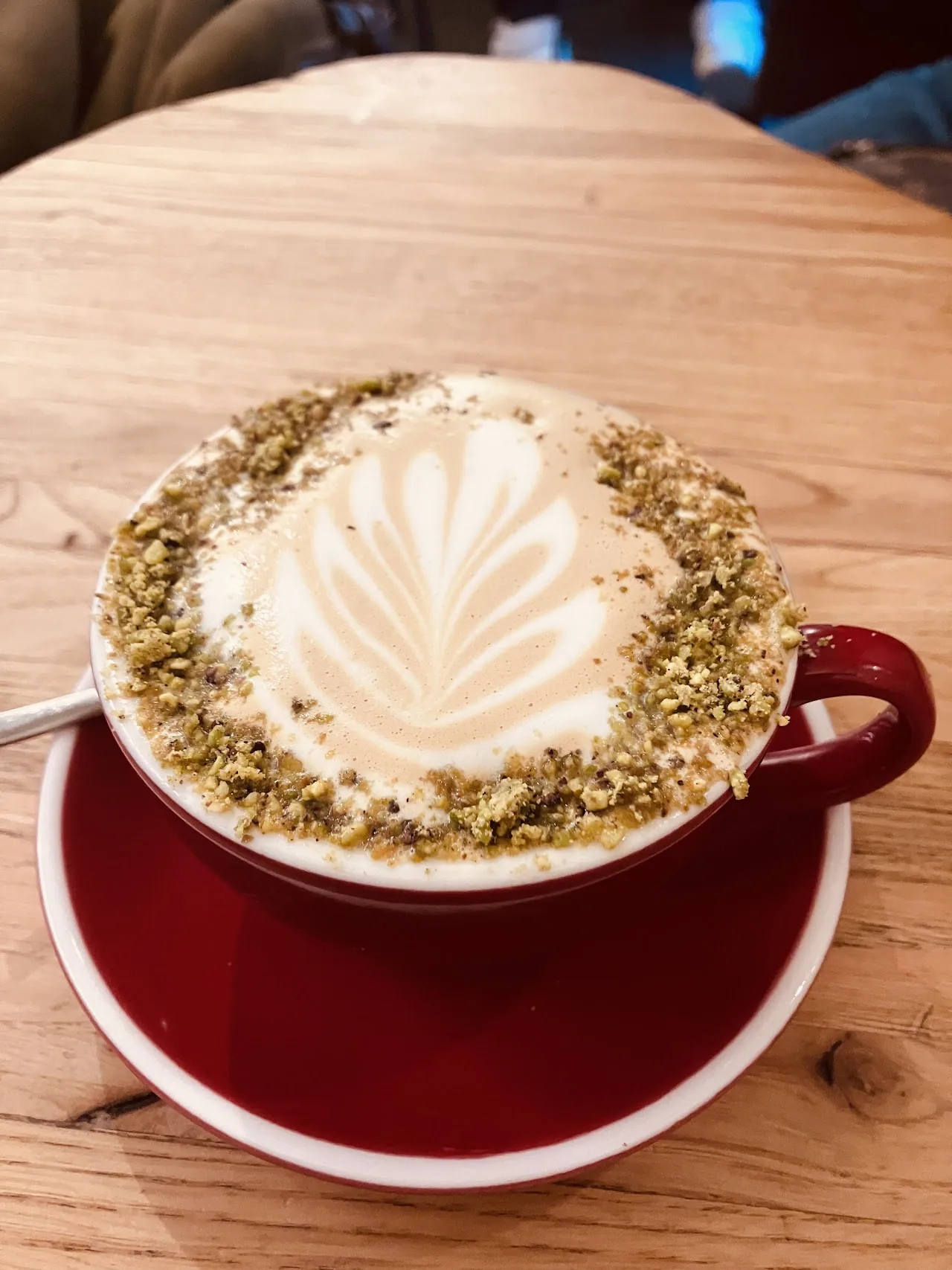 A matcha latte in a red cup with pistachio dust and latte art