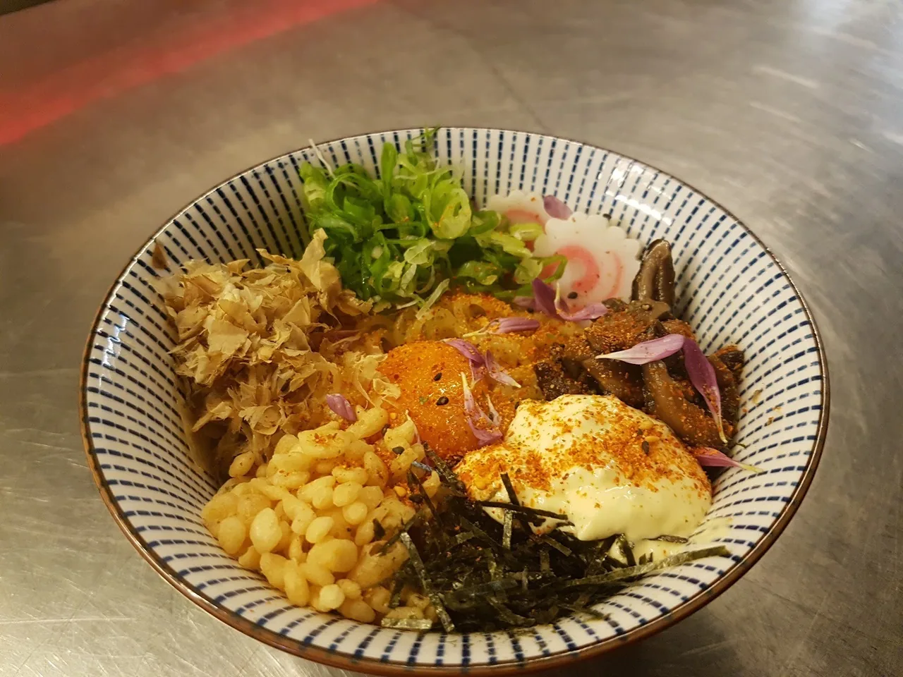 A patterned bowl of rice topped with sweetcorn, seaweed flakes, greens and a soft egg