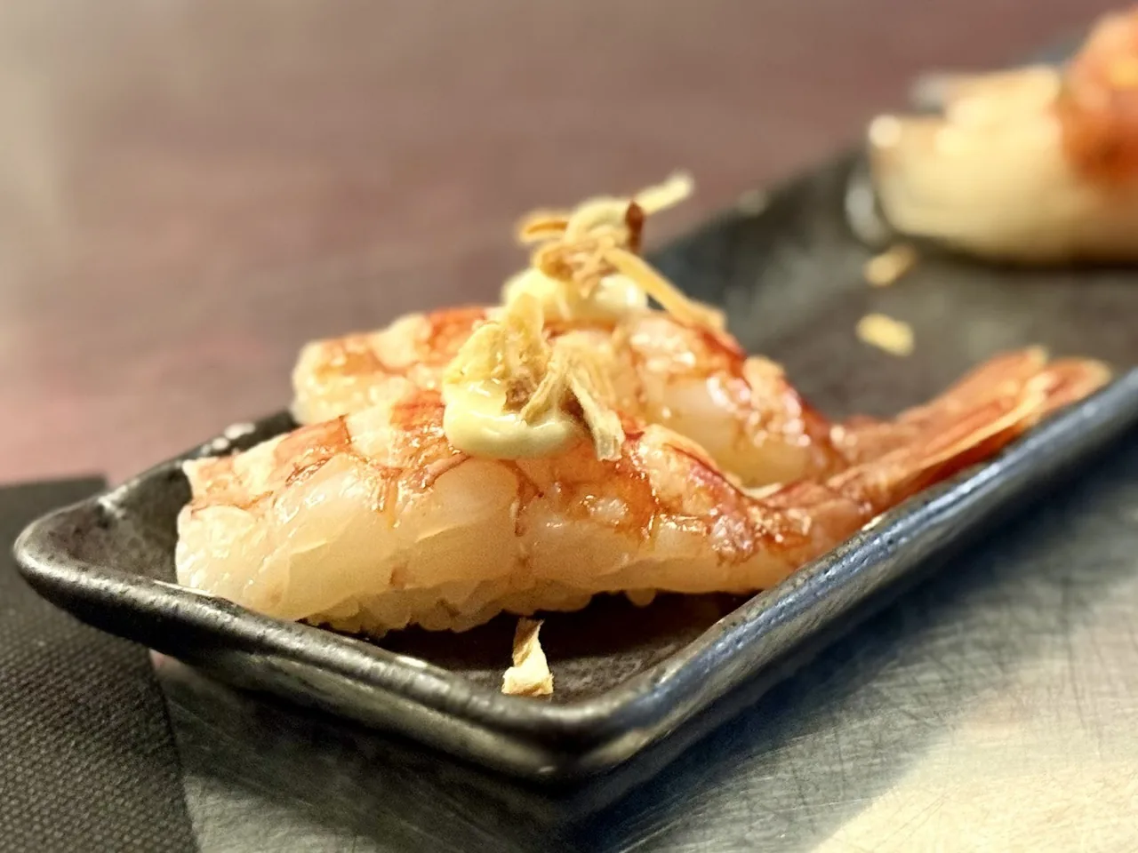 Nigiri topped with a pale prawn on a black plate