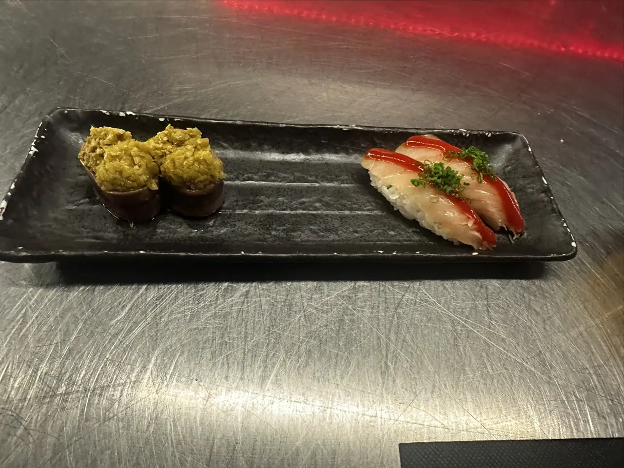Four pieces of nigiri sushi on a black rectangular plate