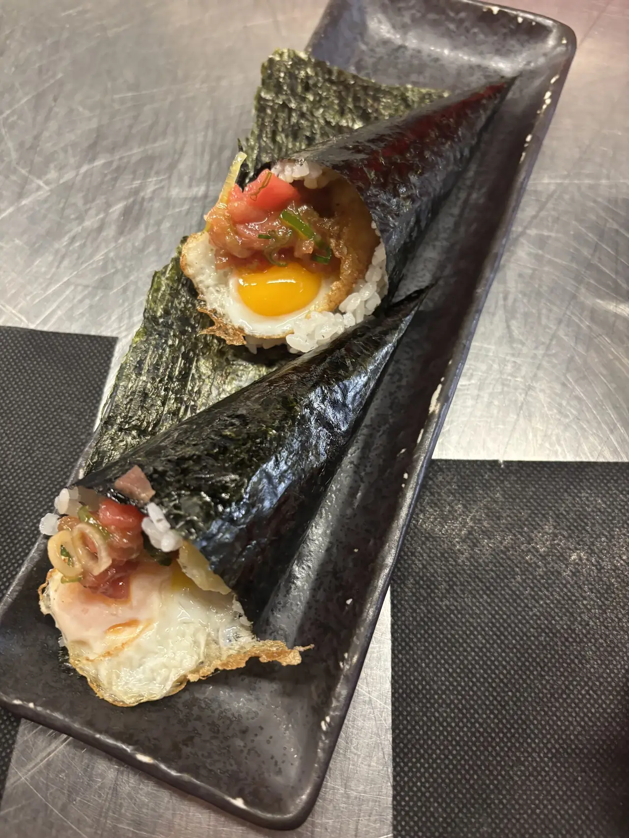Two nori hand rolls filled with rice, fried egg and diced tuna