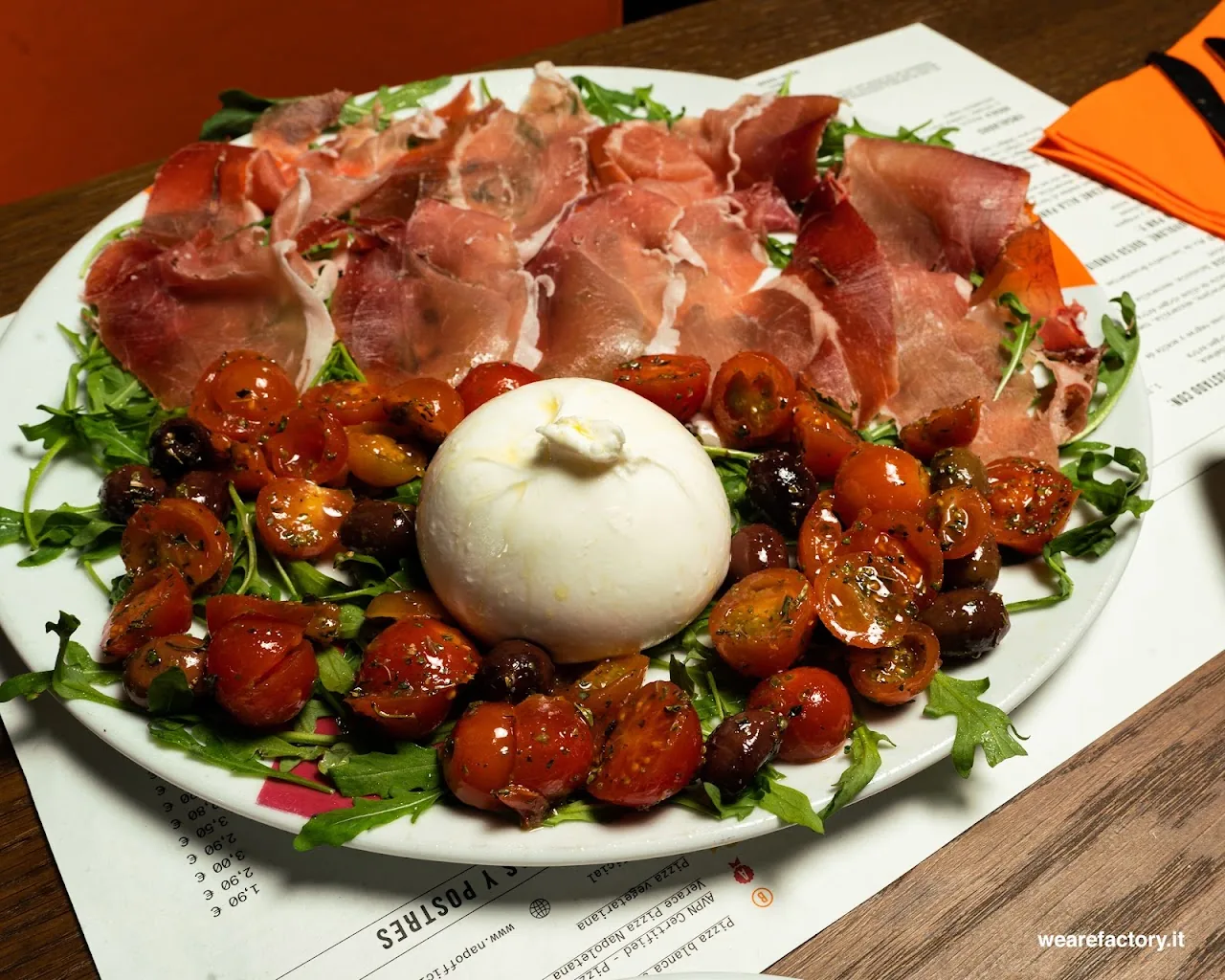 A plate of burrata with prosciutto, roasted cherry tomatoes, and arugula