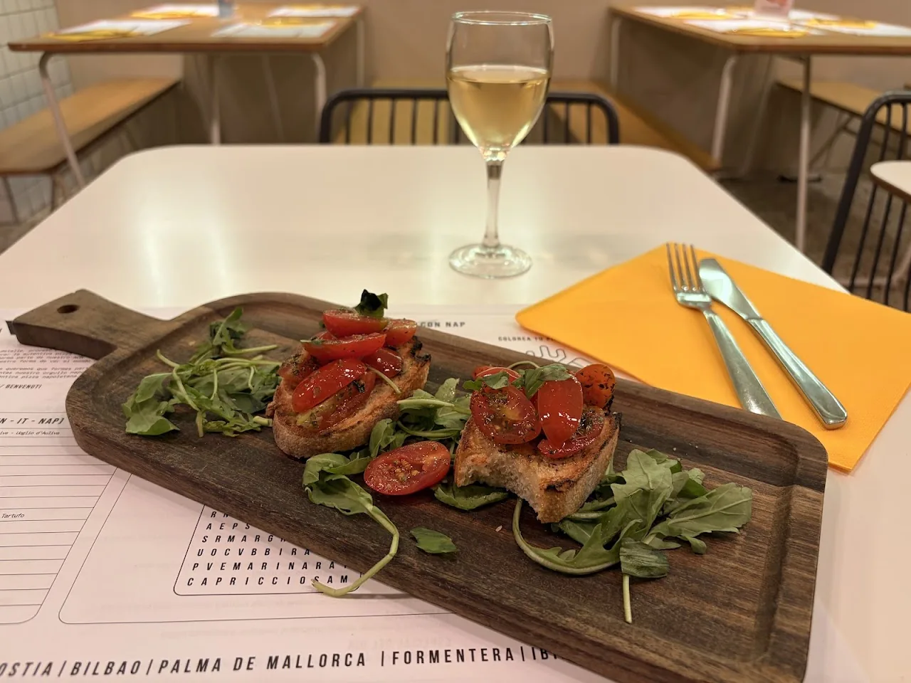 Bruschetta topped with tomato and arugula on a wooden board with wine