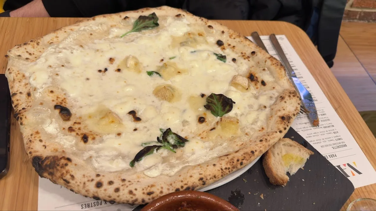 A wood-fired pizza topped with mozzarella and fresh basil leaves
