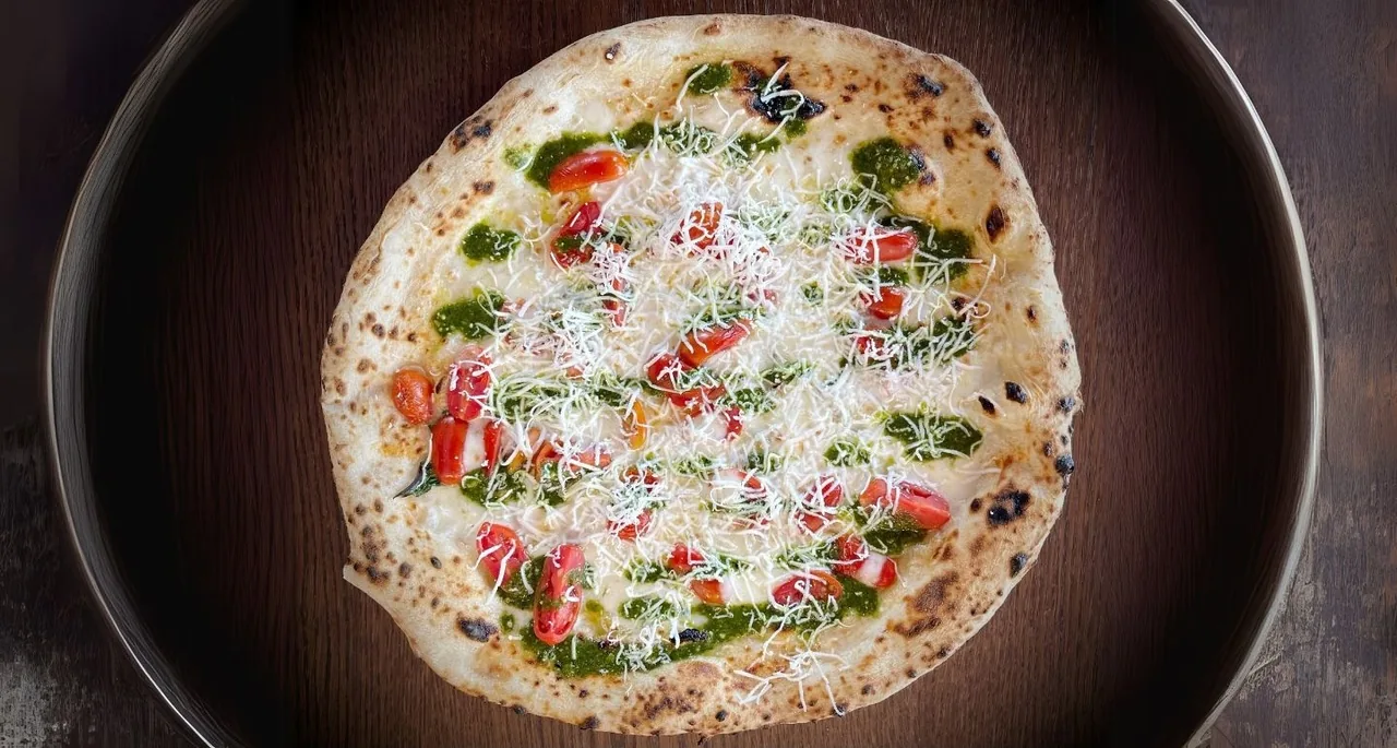 A whole pizza with white cheese and green leaves in a dark round pan